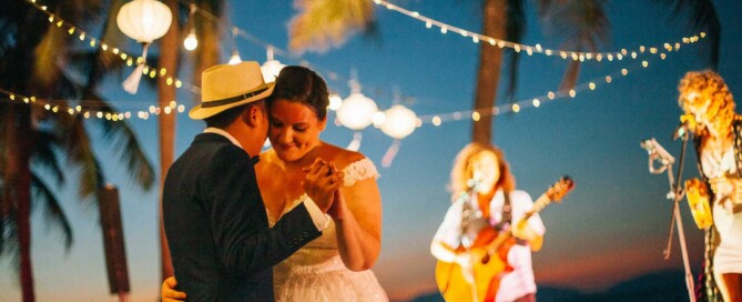 Couple dancing at beach wedding under string lights at sunset