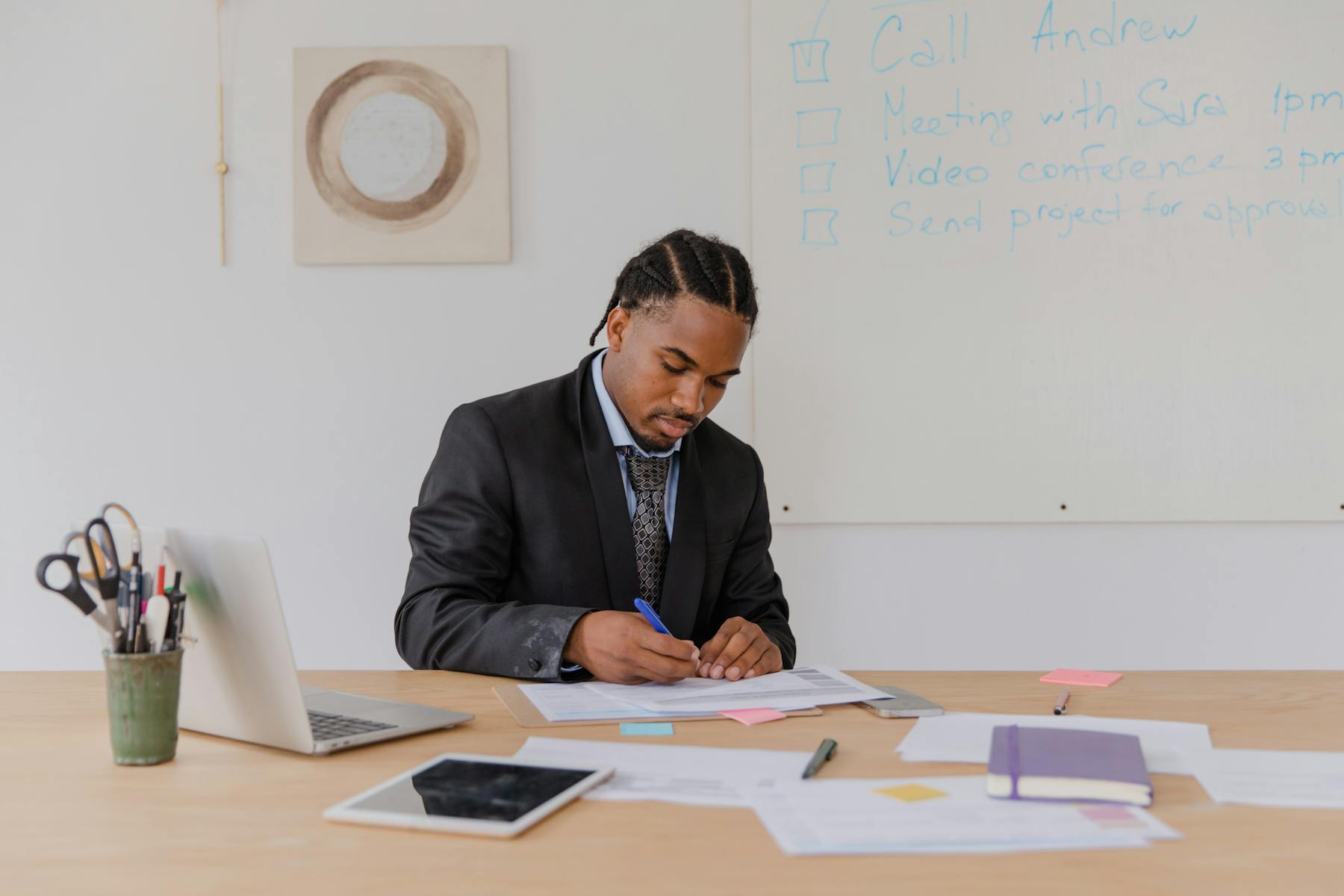 A man in a suit sits at a desk, working on a laptop in a professional office setting