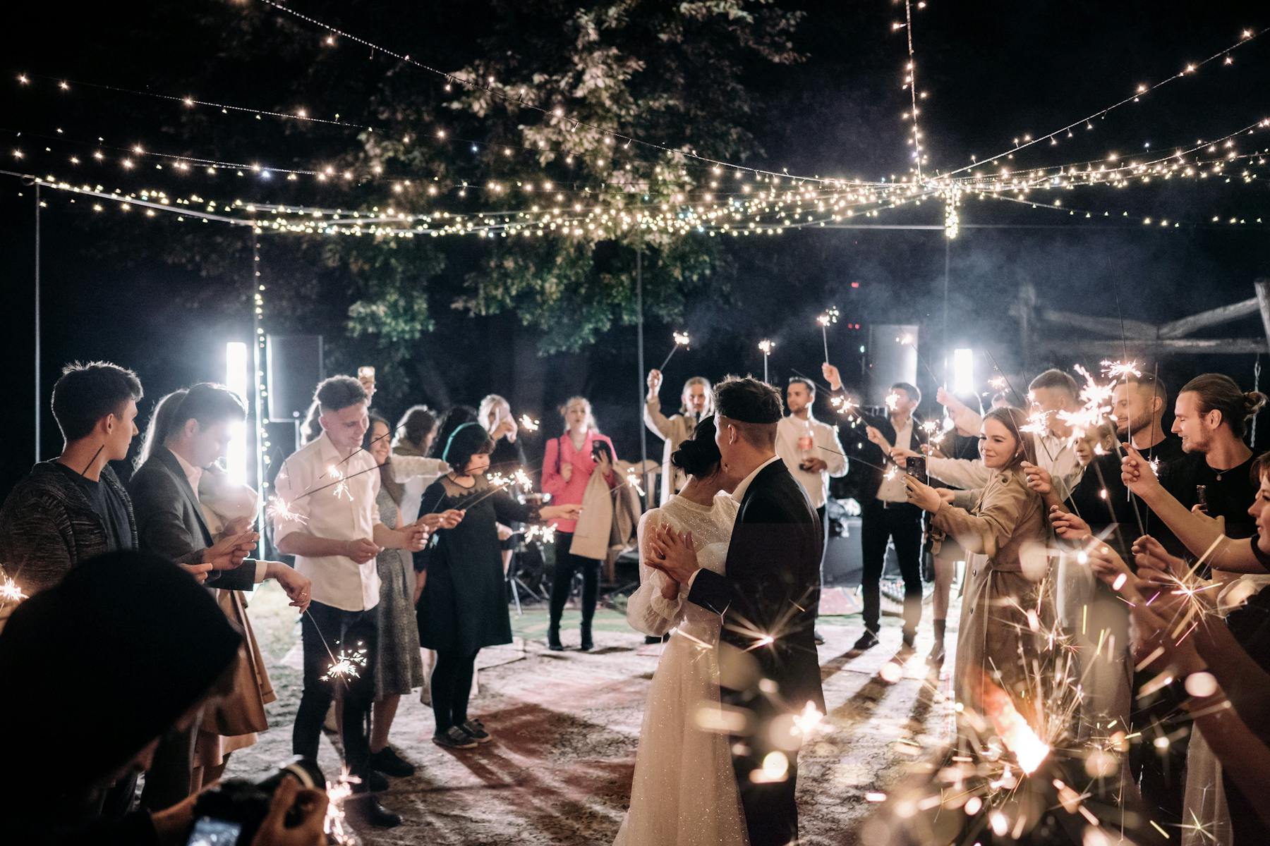 Wedding party celebrating at night, illuminated by sparklers held by guests