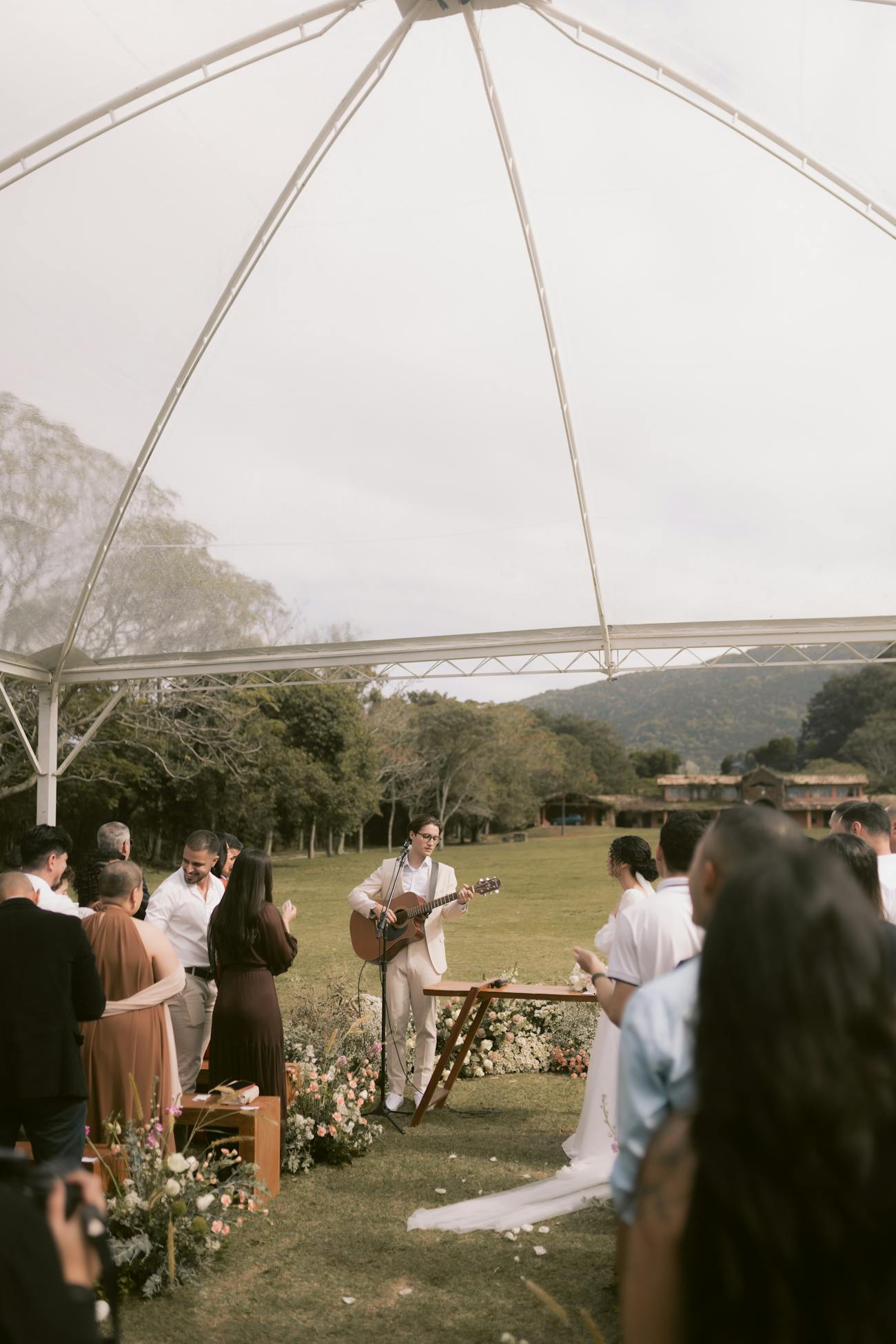 Musician playing guitar during an outdoor wedding ceremony under a tent