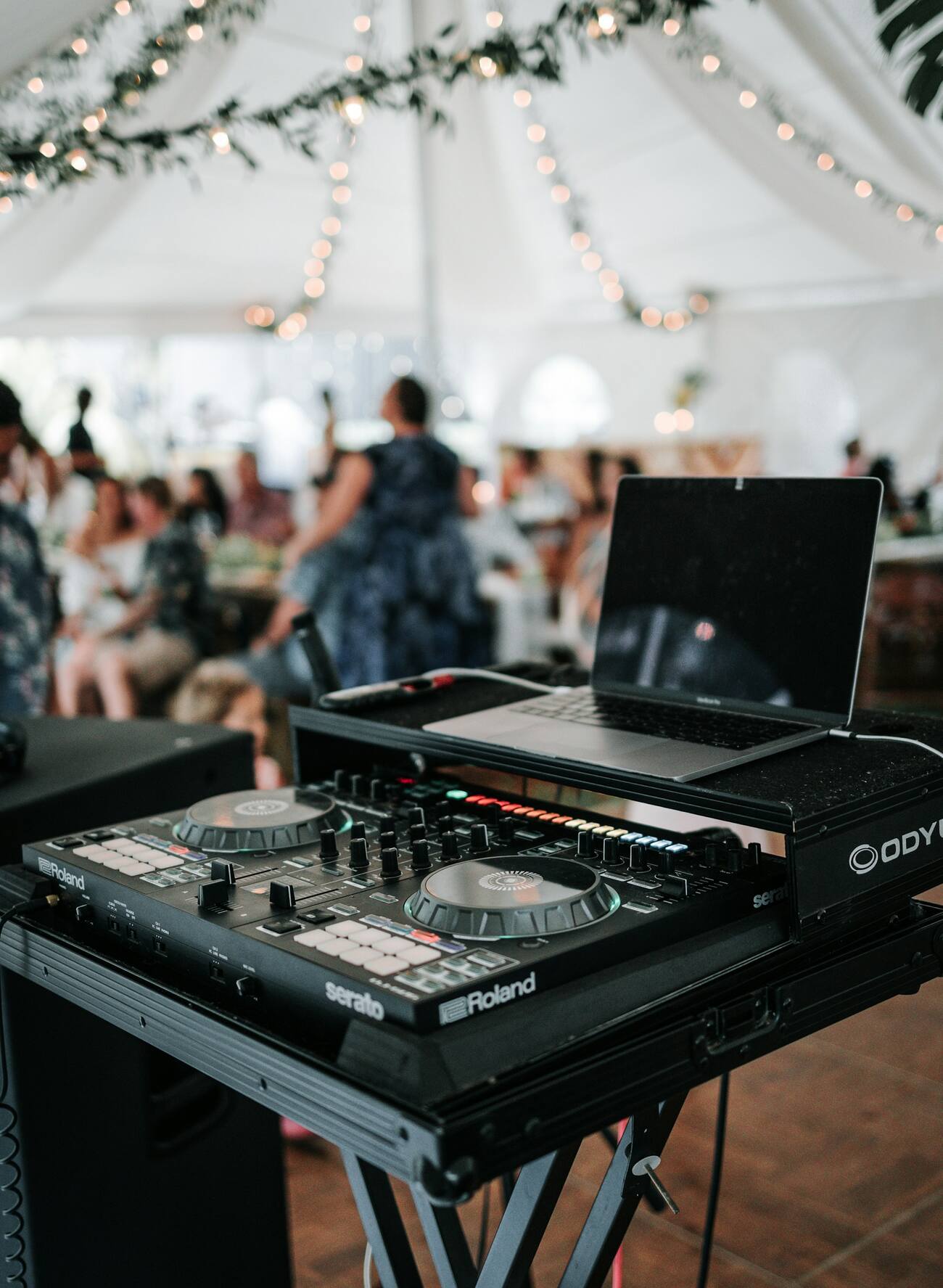 DJ controller and laptop set up under a decorated event tent with guests in the background