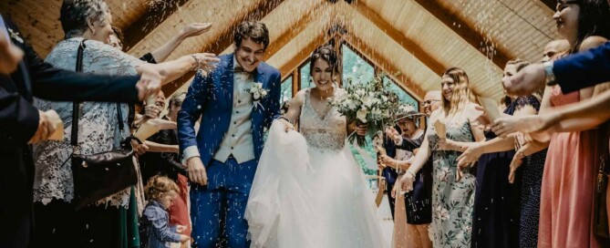 Newly married couple walking down the aisle as guests toss confetti indoors