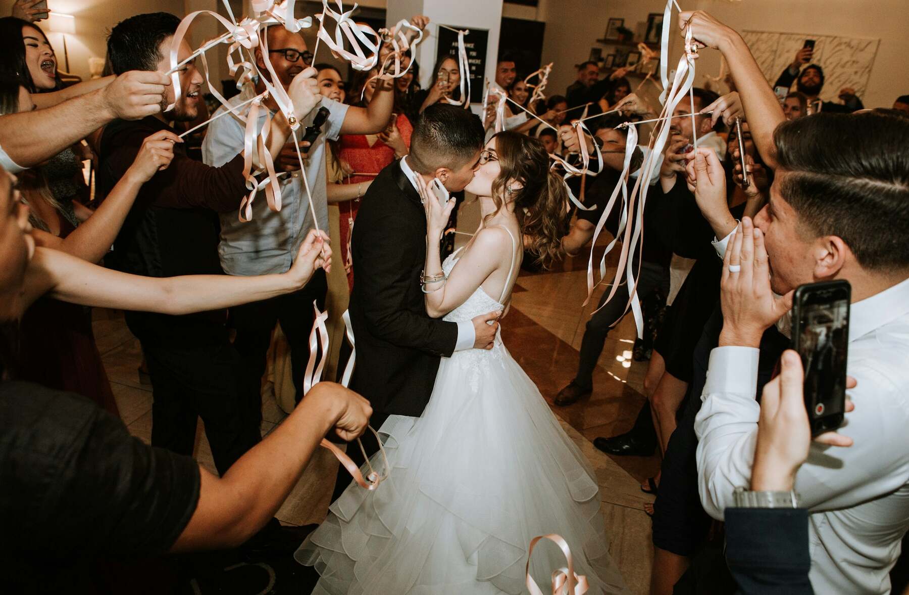 Bride and groom kissing on the dance floor surrounded by cheering guests with streamers