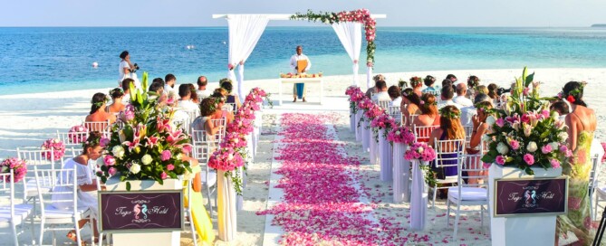 Beach wedding ceremony with floral arch and pink petal aisle by the ocean
